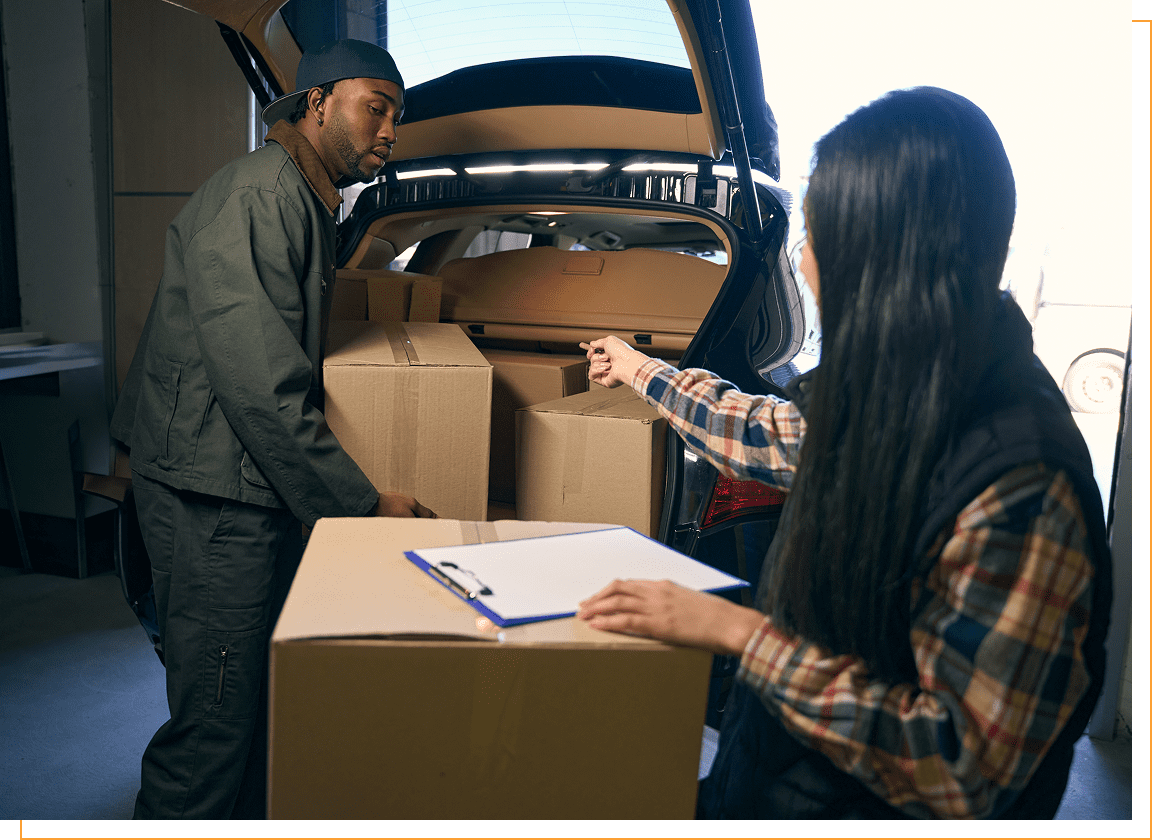 Two people loading boxes into a car.